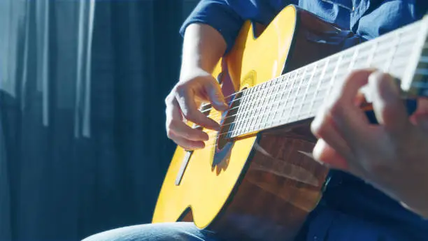 Close-up of a young man's hand playing the guitar in a room, the sun shining on the instrument