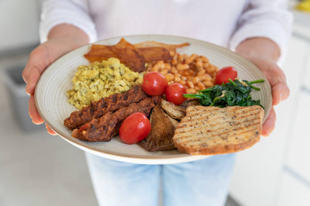 Female chef holds vegetarian breakfast Toast, vegan sausage, tofu eggs, spinach, baked beans, coconut chips, mushrooms and grape tomatoes breakfast stock pictures, royalty-free photos & images