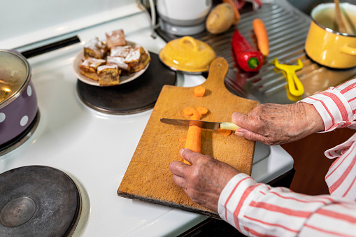 Senior woman cutting carrot on wooden cutting board. Close up of human hands