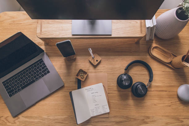 Headphones and notebook sit by smart phone, laptop and monitor, in preparation