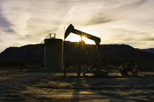 Pumpjack in Oil Field - Scenic landscape with silhouetted oil and gas extraction equipment including storage tank. Oil and gas energy industry.