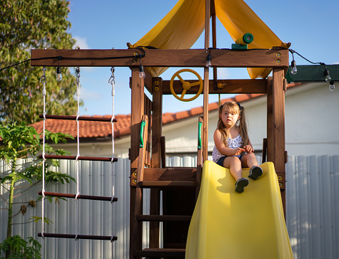 Little blond girl sitting on top of a slide in the backyard