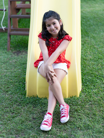 Cuban girl sitting on a slide in the playground