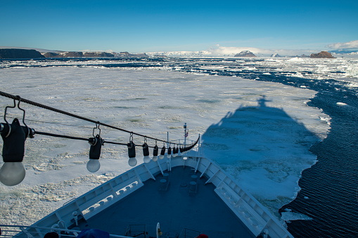The forecastle and shadow of the expedition cruise ship MS Bremen (Hapag-Lloyd Cruises) are visible in the foreground where a large stretch of sea-ice extends into the far distance, where land is visible, Weddell Sea, Antarctic Peninsula, Antarctica