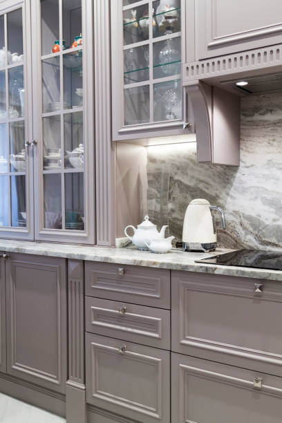 istock Modern beige and grey colored kitchen interior classic style with marble countertop in luxury apartment. cream electric kettle with porcelain tea accessories on stone countertop next to ceramic hob 1316104305