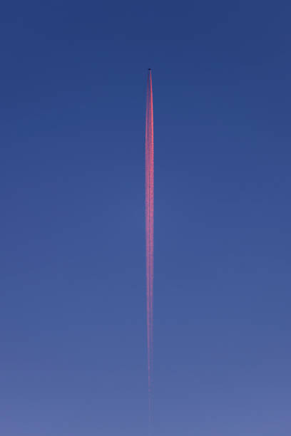 plane in the blue sky at sunrise - behind the plane a red streak of water vapor