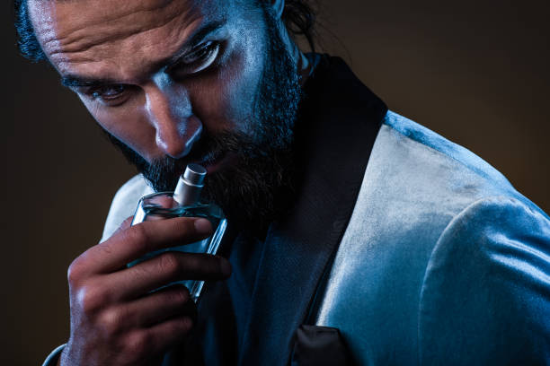 Beautiful masculine bearded young man holding a bottle of fragrance Beautiful masculine bearded young man holding a bottle of fragrance. Masculine perfume, bearded man in a suit. perfume sprayer photos stock pictures, royalty-free photos & images