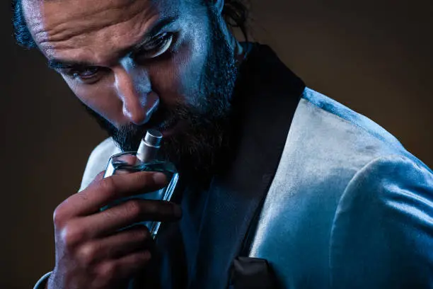 Photo of Beautiful masculine bearded young man holding a bottle of fragrance