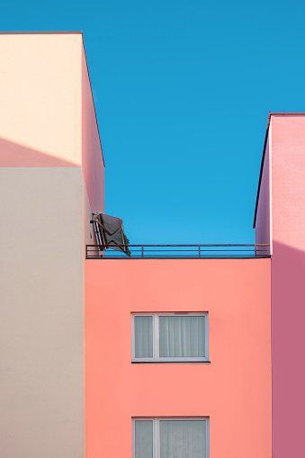 Detail residential flat apartment colorful building and minimalistic exterior of pink, purple and white color flat with balcony and sun roof on the top of it in clear blue sky background