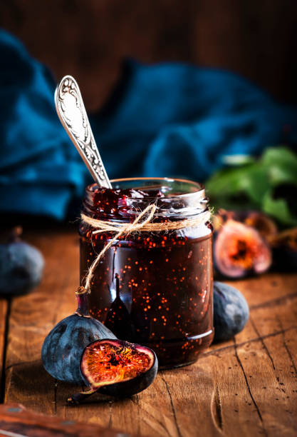 Red fig jam in jar with fresh blue figs. Homemade preparations and canning. Rustic wooden table background