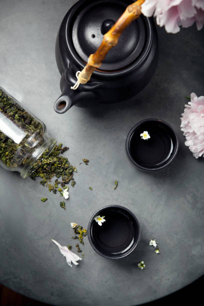 Two cups of green jasmin tea set with peonies, closeup shot Two cups of Oolong green tea with teapot, set with peionies, overview, selective focus. Dark style photo. oolong tea stock pictures, royalty-free photos & images