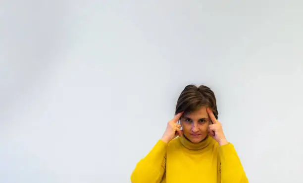 middle-aged woman in yellow sweater trying with head and hands to read mind and worried on white background with copy space and selective focus.