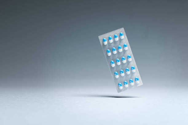 blue and white pills in a blister package hovering over a seamless background. pharmacy concept. - blister pack pill medicine healthcare and medicine imagens e fotografias de stock