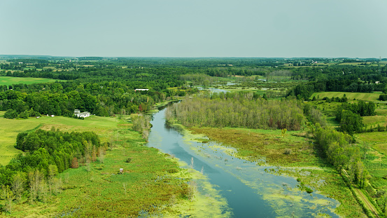 Aerial drone still of the Ahnapee River surrounded by green fields and wetlands near Forestville in Door County, Wisconsin.