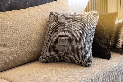 Cozy interior details. Decorative pillows in neutral colors, plaid on beige textile sofa, warm highlight. Home comfort concept, textiles, decorative accessories for apartment interior decoration.