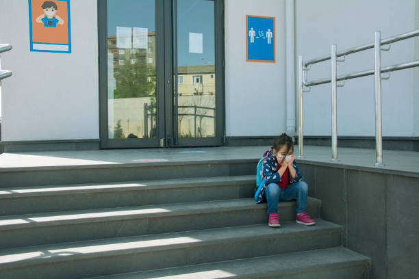 Sad little girl in protective face mask sitting on the school stairs Sad little girl in protective face mask sitting on the school stairs empty desk in classroom stock pictures, royalty-free photos & images