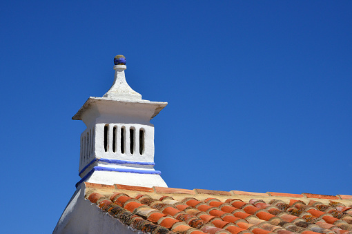 Cacela Velha, Vila Real de Santo António, Faro District, Portugal: village house with clay tiles and traditional chimney of the Algarve region, seen against blue sky.