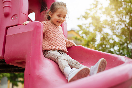 A cheerful girl with two pigtails on her head is riding a swing in the park and laughing. Emotional portrait of a child in the park