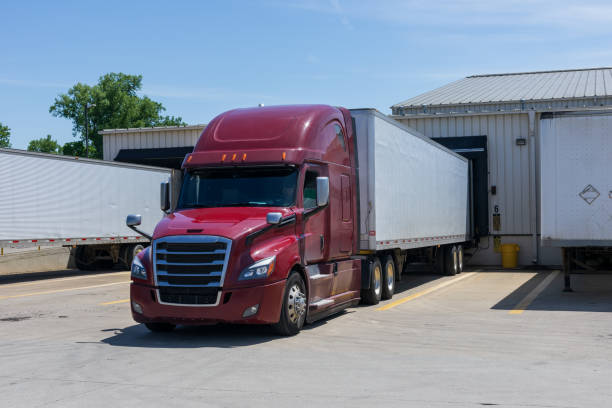 modern red big rig semi truck with a high cabin transporting a dry van semi trailer with commercial cargo are loading  at a warehouse. - distribution warehouse industrial building large building exterior imagens e fotografias de stock