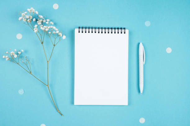 White sheet of notebook on a blue background and a sprig of flowers White sheet of notebook on a blue background and a sprig of flowers. Beautiful spring background. Plans for the summer. Copyspace for congratulations. Small white gypsophila flowers. white shabby chic desk stock pictures, royalty-free photos & images