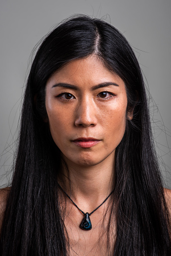 Serious asian mid adult woman looking at the camera on gray background