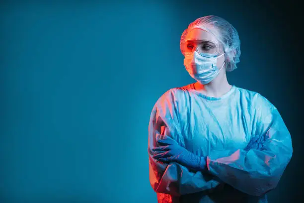 Covid-19 outbreak. Pandemic banner. Respiratory infection risk. Portrait of disturbed pensive female doctor in ppe face mask goggles looking at copy space isolated on dark blue background.