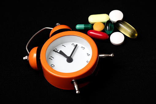 Close-Up Of Clock And Pills Against Black Background