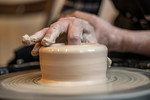 A man in old medieval Byzantine clothes sits behind a vintage potter's wheel and makes dishes out of clay. Pottery in nature in retro style.