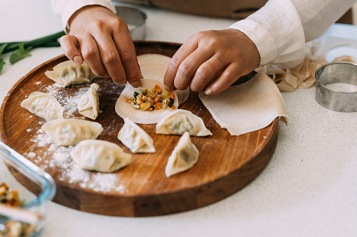 Horizontal shot of an anonymous chef's hands filling dumplinggyoza wrappers on a wooden plate