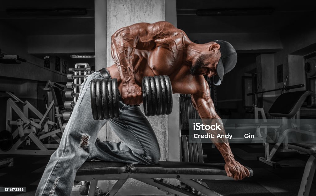 Muscular man pulls a dumbbell towards his stomach. Bodybuilding and powerlifting concept. Muscular man pulls a dumbbell towards his stomach. Bodybuilding and powerlifting concept. Mixed media Body Building Stock Photo