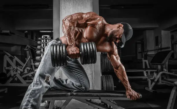 Photo of Muscular man pulls a dumbbell towards his stomach. Bodybuilding and powerlifting concept.