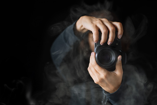 Woman's hands held photo camera. Close up shot. A person in black hoodie and smoke around.