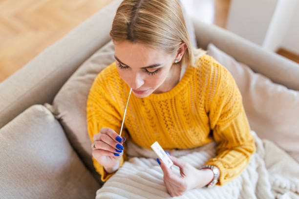 istock woman using cotton swab while doing coronavirus PCR test at home. Woman using coronavirus rapid diagnostic test. Young woman at home using a nasal swab for COVID-19. 1316184126