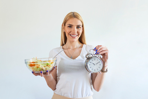 Young woman holding clock and Healthy food of salad Intermittent fasting concept. Time to lose weight , eating control or time to diet concept.