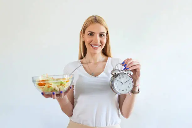 Young woman holding clock and Healthy food of salad Intermittent fasting concept. Time to lose weight , eating control or time to diet concept.