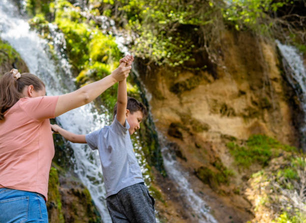 istock Mother with son enjoying the mountain, standing under the waterfall 1316186319