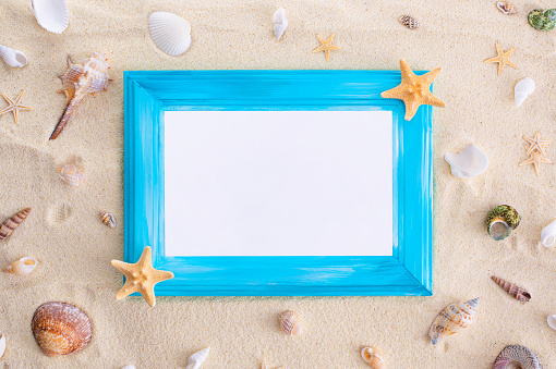 Summer vacation mockup:Blue wooden frame with white paper sheet, seashells and starfish on sand background. Travel, beach concept. Copy space. Sea Flat lay.