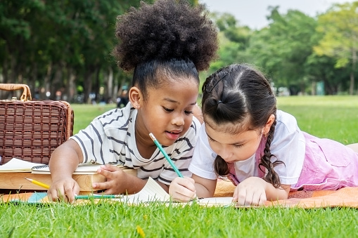 Dos niñas africanas americanas acostadas y dibujando con lápices de colores en el parque de verano, sienten felicidad, conceptos de educación al aire libre photo