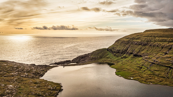 Leitisvatn Sunset. Lonely Boat at Bosdalafossur at Sørvágsvatn Lake (Leitisvatn), Sorvagsvatn the largest lake in the Faroe Islands. Panorama View of Sørvágsvatn around 40 metres above the level of sea. Surrounded by higher cliff and hill range prevents it from emptying fully into the ocean, lonely boat anchored close to Bøsdalafossur waterfall being the outlet into the north atlantic ocean. Vágar Island, Faroe Islands, Denmark, Nordic Countries, Europe