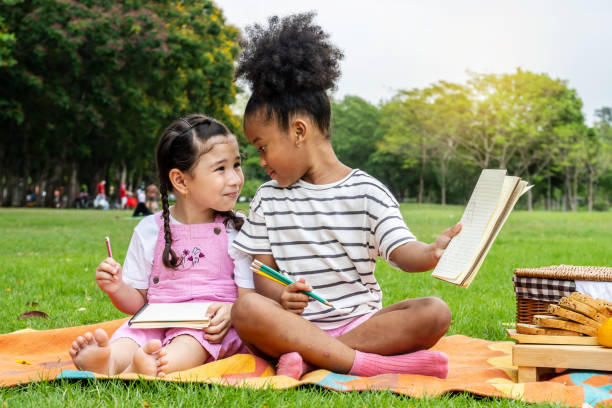 istock Two African American little girl using pencil writing and doing homework on notebook together while sitting and lying on mat outdoor in the park 1316195224