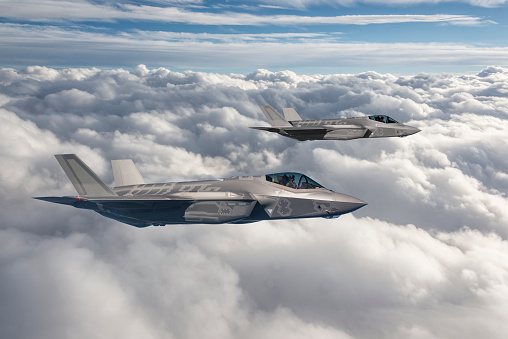 Two fighter jets flying over clouds