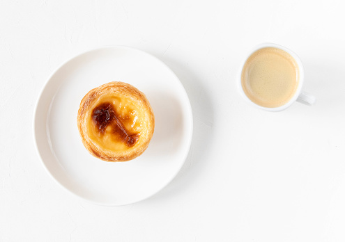 Pastel de nata - traditional cream cake from Portugal on a plate with a cup of coffee - morning breakfast dessert concept - top view, white background