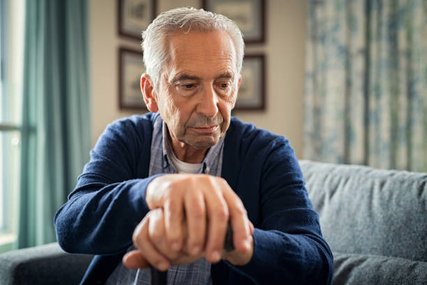 Depressed senior man with stick Depressed old man sitting at home while holding walking stick. Retired sad man holding wooden walking cane handle sitting alone at care facility. Elderly man suffering from loneliness and alzheimer at nursing home. parkinsons disease photos stock pictures, royalty-free photos & images