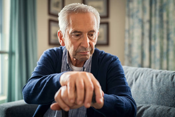 Depressed senior man with stick Depressed old man sitting at home while holding walking stick. Retired sad man holding wooden walking cane handle sitting alone at care facility. Elderly man suffering from loneliness and alzheimer at nursing home. old man depressed stock pictures, royalty-free photos & images