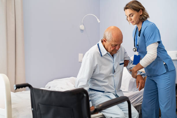 Nurse helping senior patient at clinic Lovely nurse assisting senior man to get up from bed at hospital. Caring nurse supporting elderly patient while getting up from bed and move towards wheelchair at nursing home. Disabled man standing up at care centre while caregiver helping him to get up in the morning. hospital patient bed nurse stock pictures, royalty-free photos & images