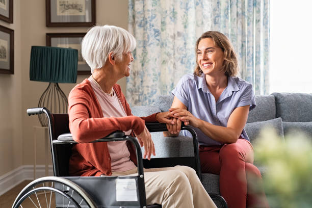 Happy adult woman visiting her elderly mother at home Mature woman comforting senior mom sitting on wheelchair at nursing home. Cheerful woman talking to old disabled mother in wheelchair at elder care centre. Loving caregiver taking care of elderly woman at home. social services stock pictures, royalty-free photos & images