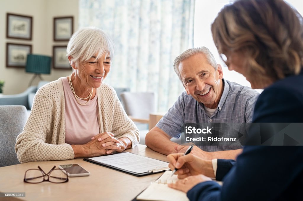 Senior couple consulting with financial agent Senior couple planning their investments with financial advisor at home. Happy aged couple planning their medical insurance with advisor in living room. Old couple consulting with insurance agent while sitting together at home. Senior Adult Stock Photo