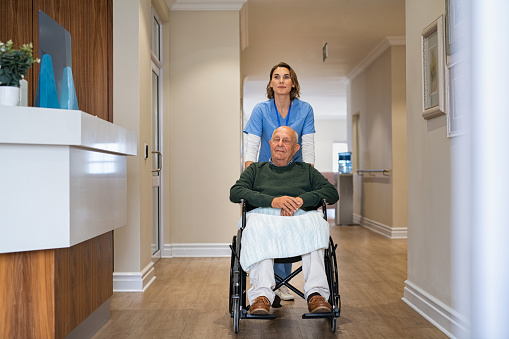 Enfermera empujando a hombre mayor en silla de ruedas en clínica privada photo