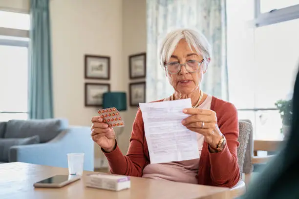 Senior woman checking prescription and dosage of medicine. Elderly lady with spectacles reading medical instructions before taking medicine at home. Senior woman reading side effects list of drug and contraindications of the package leaflet prescribed by the doctor.