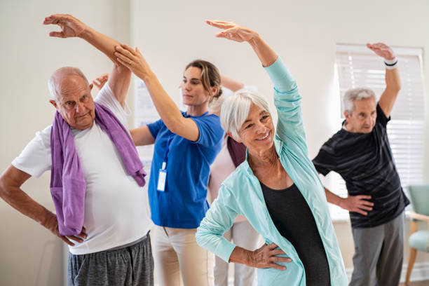 senioren strecken sich mit trainer in der seniorengemeinschaft - senior adult exercising aging process instructor stock-fotos und bilder